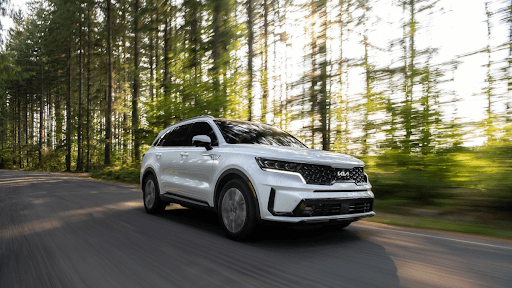 SUV Kia blanco en movimiento por carretera rodeada de bosque, equipado con llantas Yokohama para alt