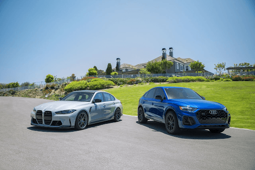 BMW M3 gris y Audi SQ5 azul estacionados uno al lado del otro en una calle residencial, ambos equipa