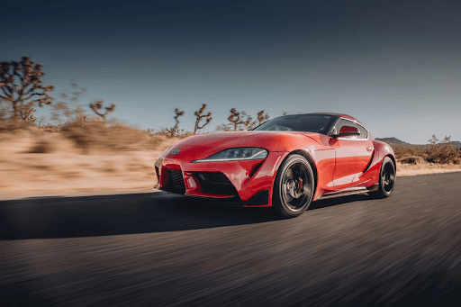 Toyota Supra rojo en movimiento por carretera desértica, equipado con llantas Yokohama ADVAN Apex V6