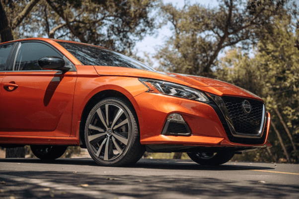 Vista de tres cuartos delanteros de un Nissan Altima naranja estacionado en una calle rodeada de árb