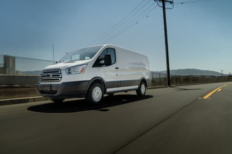 Furgoneta blanca Ford Transit en movimiento por una carretera, con fondo de paisaje montañoso y ciel