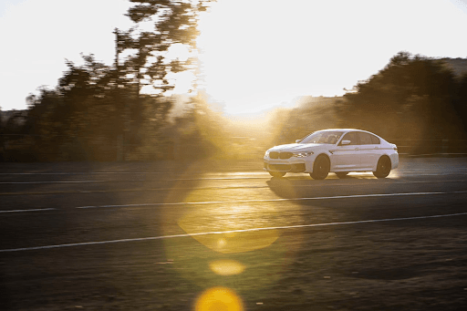 Auto deportivo BMW M5 blanco conduciendo a alta velocidad en carretera al atardecer, con destellos d