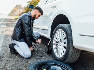 Persona utilizando un gato hidráulico para levantar un automóvil antes de cambiar la llanta.